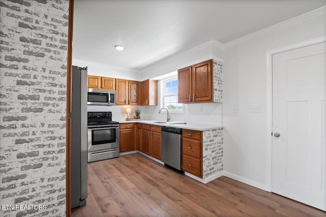 kitchen with a sink, ornamental molding, wood finished floors, stainless steel appliances, and decorative backsplash