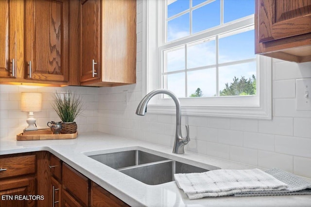 kitchen featuring brown cabinetry, tasteful backsplash, a sink, and plenty of natural light