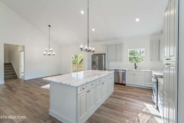kitchen with an inviting chandelier, a sink, appliances with stainless steel finishes, light wood-style flooring, and a kitchen island