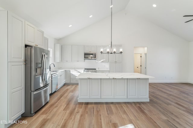 kitchen with high vaulted ceiling, a kitchen island, light wood-style floors, and appliances with stainless steel finishes