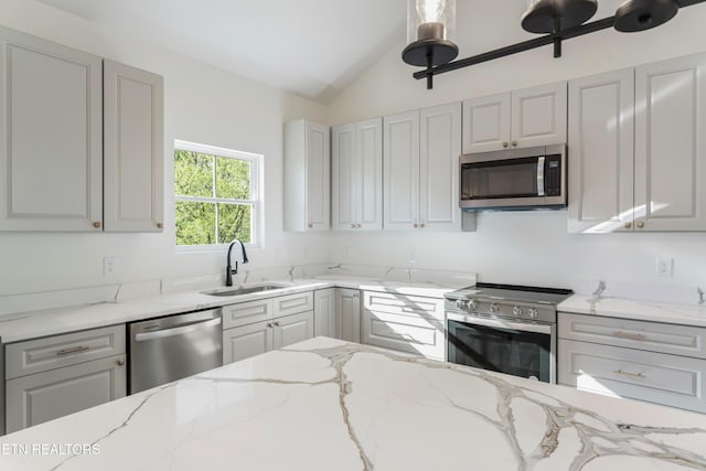 kitchen with a sink, light stone countertops, appliances with stainless steel finishes, and lofted ceiling