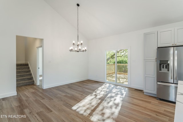 unfurnished dining area with high vaulted ceiling, light wood finished floors, a chandelier, and stairs