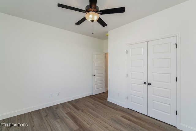 unfurnished bedroom featuring ceiling fan, a closet, baseboards, and wood finished floors