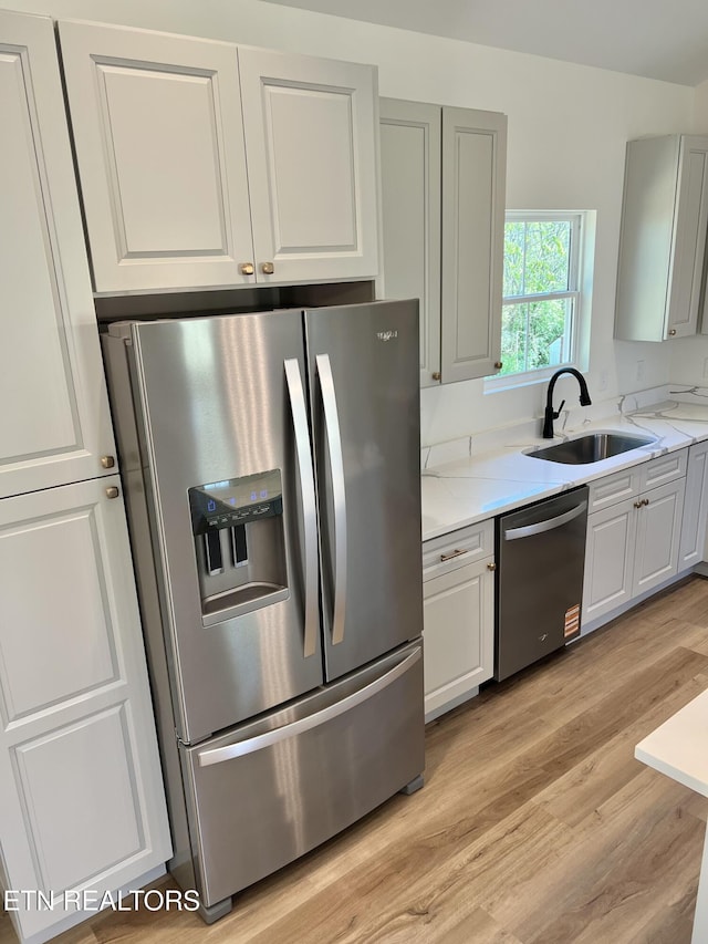 kitchen with light wood-style flooring, white cabinetry, light stone countertops, stainless steel appliances, and a sink
