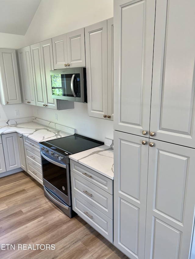 kitchen featuring light wood-type flooring, appliances with stainless steel finishes, vaulted ceiling, and light stone countertops