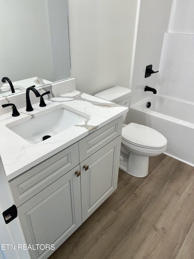 bathroom with toilet, wood finished floors, vanity, and  shower combination