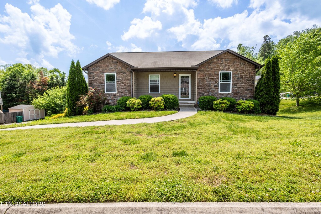 single story home featuring a storage shed, an outbuilding, a front yard, and stone siding