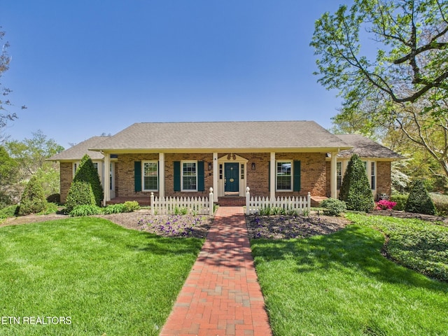 ranch-style house with roof with shingles, a front yard, brick siding, and covered porch