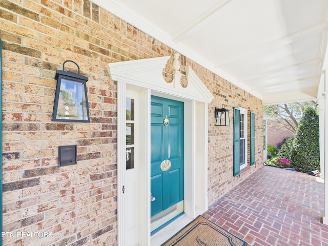 doorway to property with covered porch and brick siding