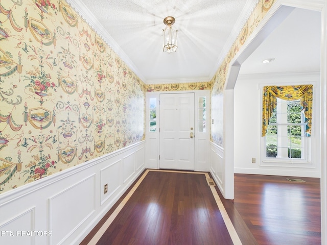 entrance foyer with crown molding, a decorative wall, dark wood-type flooring, a wainscoted wall, and wallpapered walls