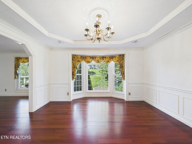 empty room featuring a decorative wall, a notable chandelier, wood finished floors, and crown molding