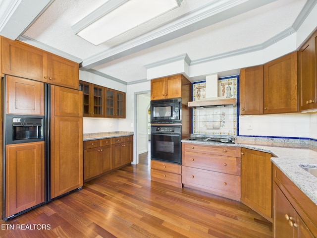 kitchen featuring premium range hood, brown cabinets, black appliances, wood finished floors, and decorative backsplash