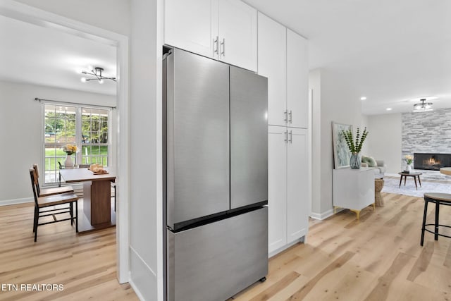 kitchen featuring baseboards, a stone fireplace, light wood-style floors, white cabinetry, and stainless steel refrigerator