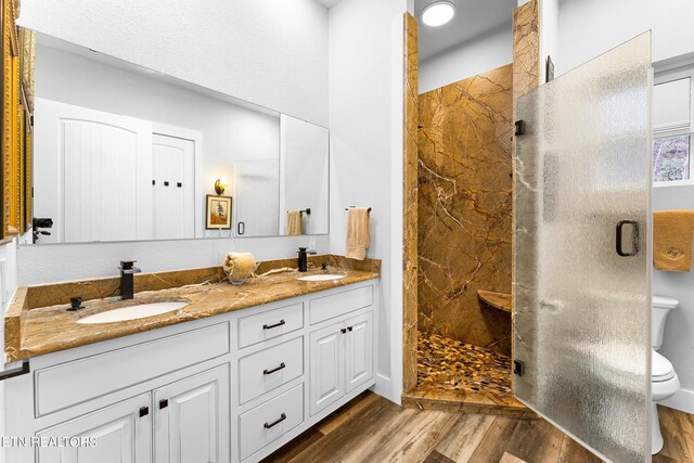 full bath with toilet, a walk in shower, wood finished floors, and double vanity