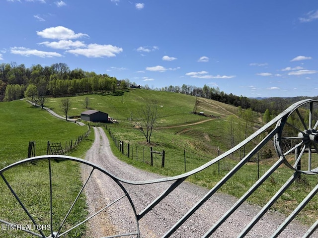 view of property's community with a yard, a rural view, fence, and driveway