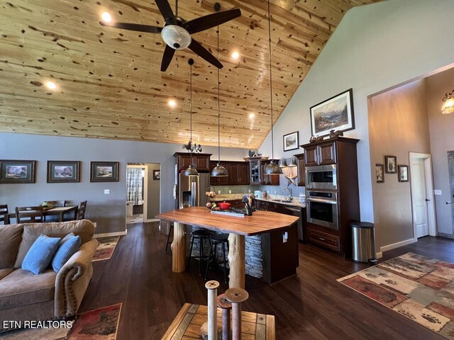 kitchen featuring dark brown cabinetry, appliances with stainless steel finishes, high vaulted ceiling, an island with sink, and wooden counters