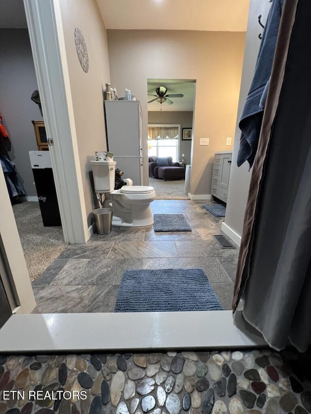 bathroom with toilet, ceiling fan, stone finish flooring, and baseboards