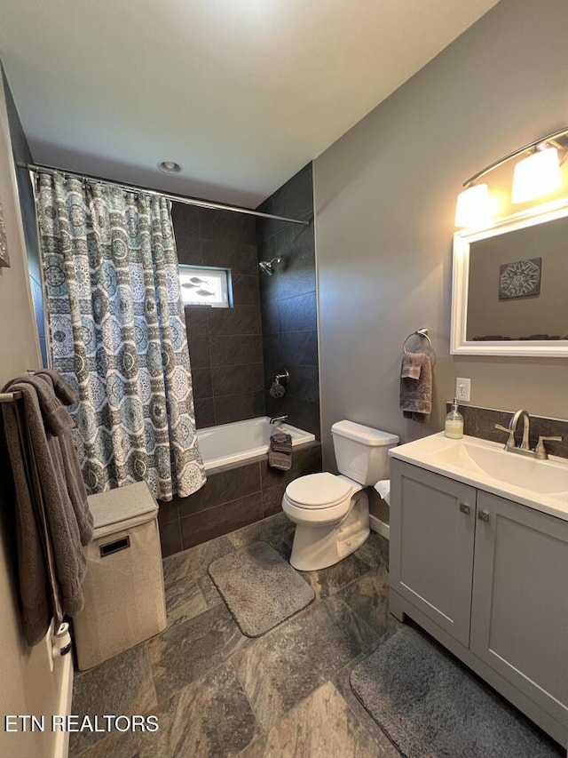 full bathroom with vanity, toilet, baseboards, tiled shower / bath combo, and stone finish flooring