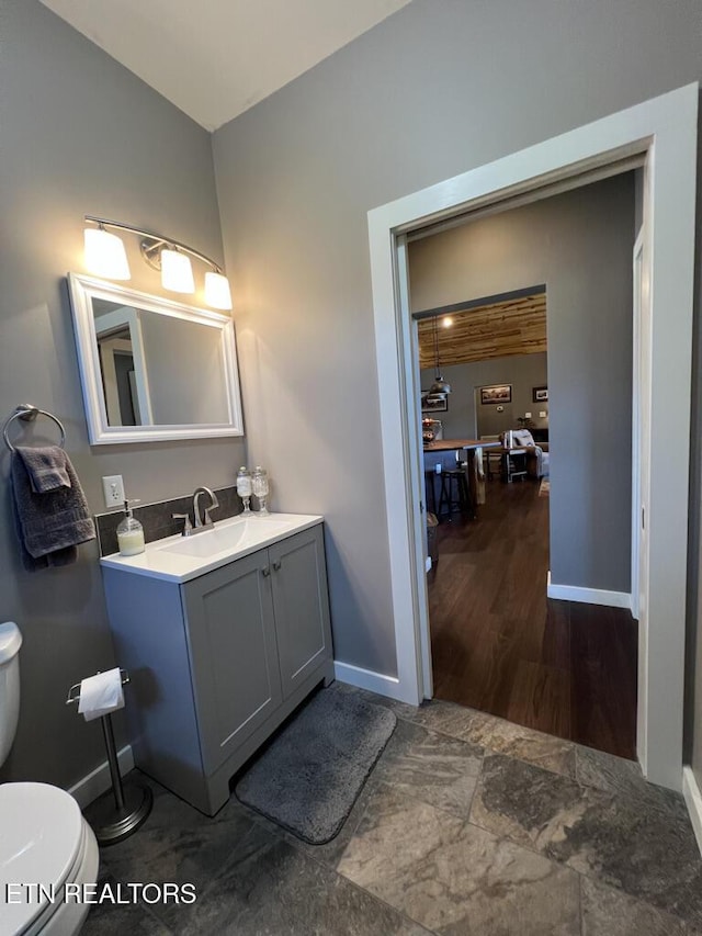 half bathroom with baseboards, toilet, and vanity