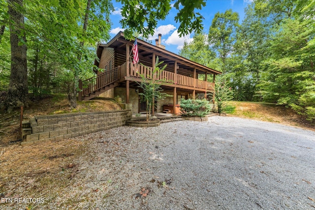 view of front facade with stairs, a deck, log siding, and a chimney