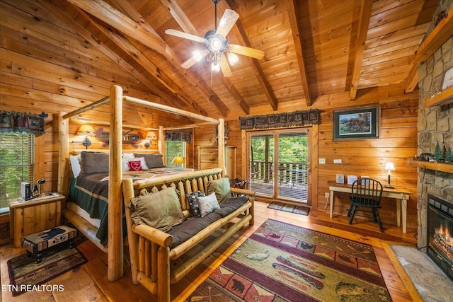 bedroom featuring wood-type flooring, a stone fireplace, vaulted ceiling with beams, and wooden walls