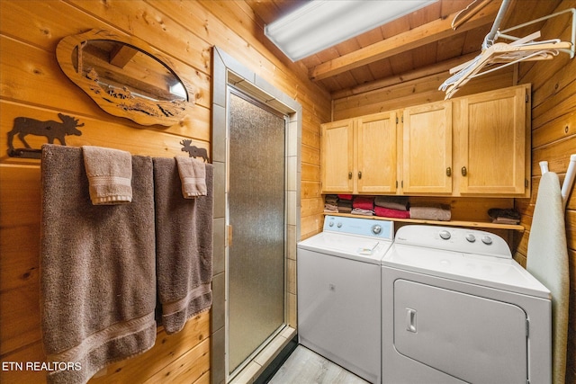 laundry room featuring light wood-style flooring, wood walls, cabinet space, and washing machine and dryer