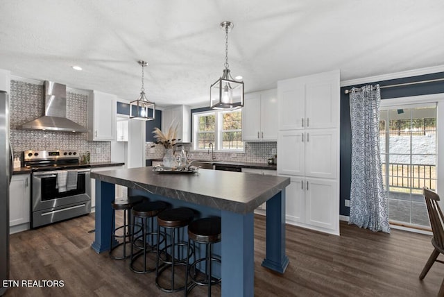 kitchen featuring dark wood-type flooring, dark countertops, wall chimney exhaust hood, and stainless steel range with electric cooktop