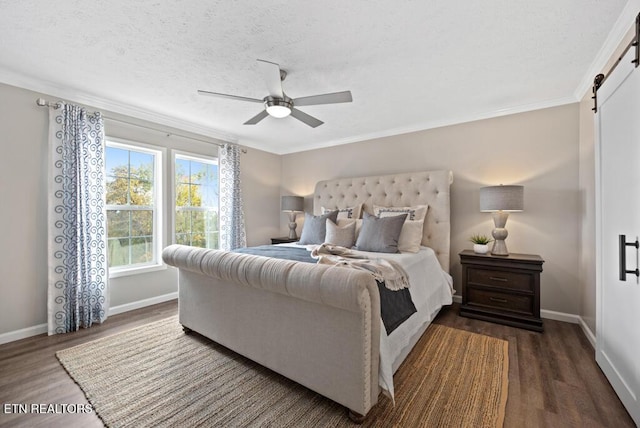 bedroom featuring crown molding, dark wood finished floors, a ceiling fan, a barn door, and baseboards