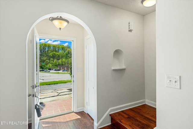 foyer with dark wood-type flooring, arched walkways, and baseboards