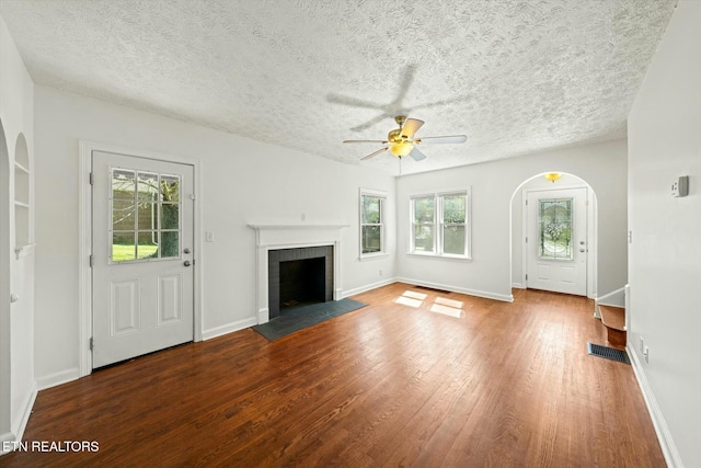 unfurnished living room featuring arched walkways, a ceiling fan, plenty of natural light, and wood finished floors