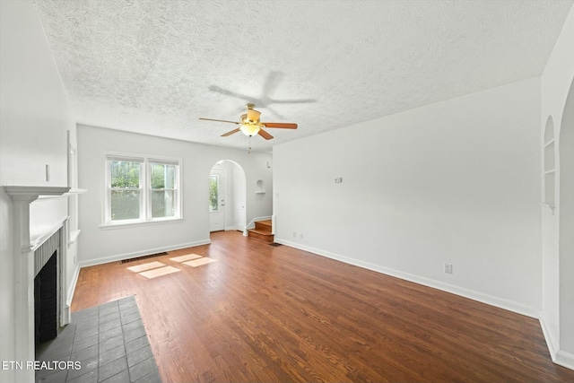 unfurnished living room with arched walkways, a fireplace with flush hearth, a textured ceiling, and a ceiling fan