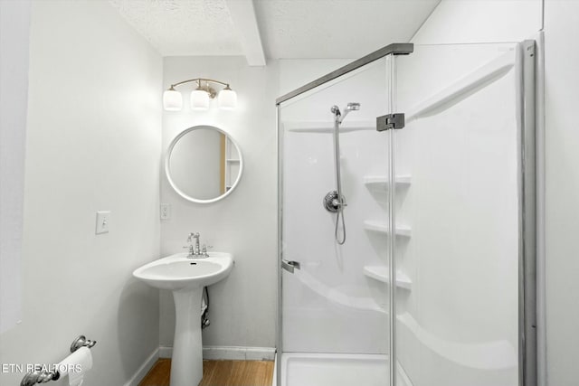 full bathroom with a shower stall, a textured ceiling, wood finished floors, baseboards, and beam ceiling