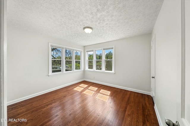empty room with a textured ceiling, wood finished floors, and baseboards