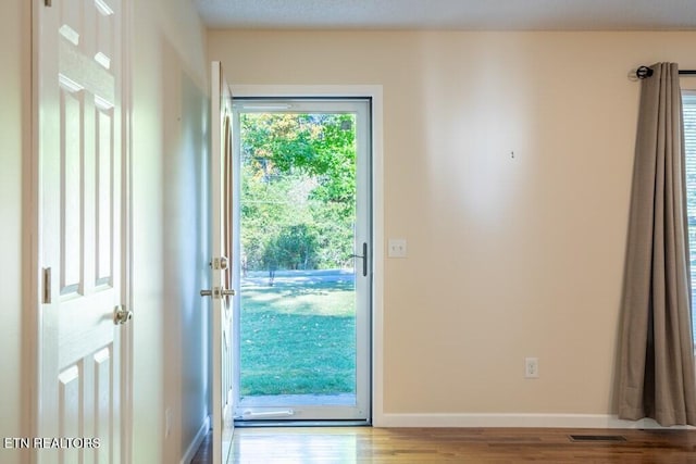 doorway to outside featuring visible vents, baseboards, and wood finished floors