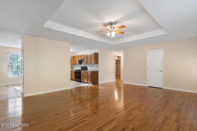 unfurnished living room featuring light wood-type flooring, a tray ceiling, baseboards, and ceiling fan
