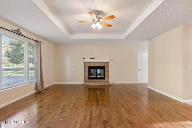 unfurnished living room featuring baseboards, a raised ceiling, a tiled fireplace, ceiling fan, and wood finished floors