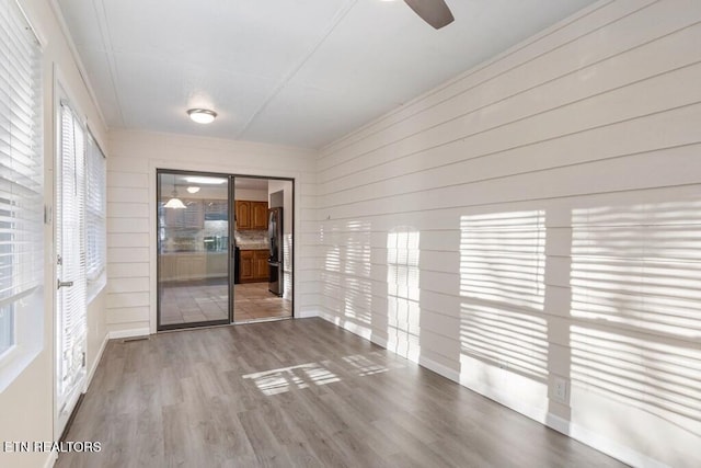 spare room featuring wood walls, visible vents, light wood-type flooring, and ceiling fan