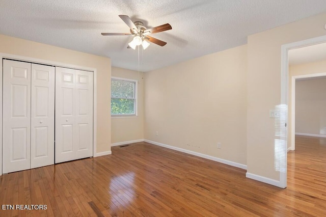 unfurnished bedroom with a closet, baseboards, a textured ceiling, and wood finished floors