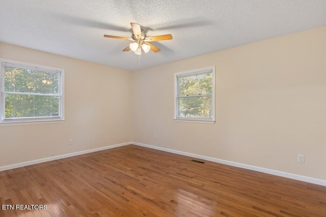empty room featuring ceiling fan, a textured ceiling, visible vents, wood finished floors, and baseboards
