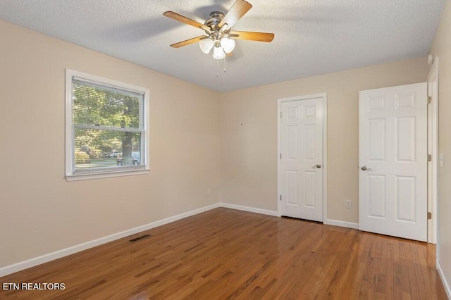 unfurnished bedroom with baseboards, a textured ceiling, a ceiling fan, visible vents, and wood finished floors