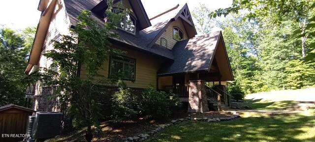 view of side of home with roof with shingles, central AC, and a lawn