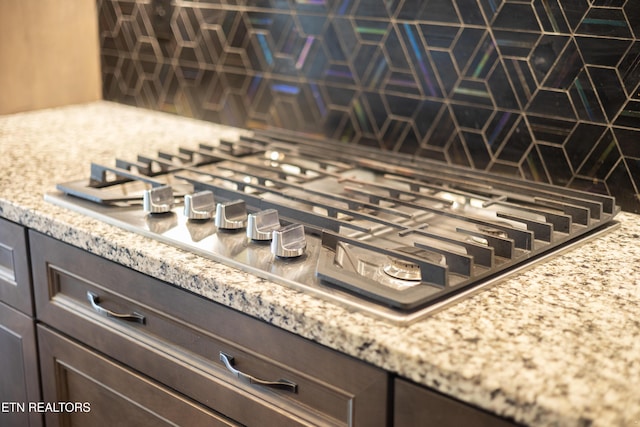 details featuring light stone counters, decorative backsplash, dark brown cabinetry, and stainless steel gas cooktop