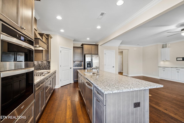kitchen with light stone counters, ornamental molding, appliances with stainless steel finishes, and dark wood-style floors