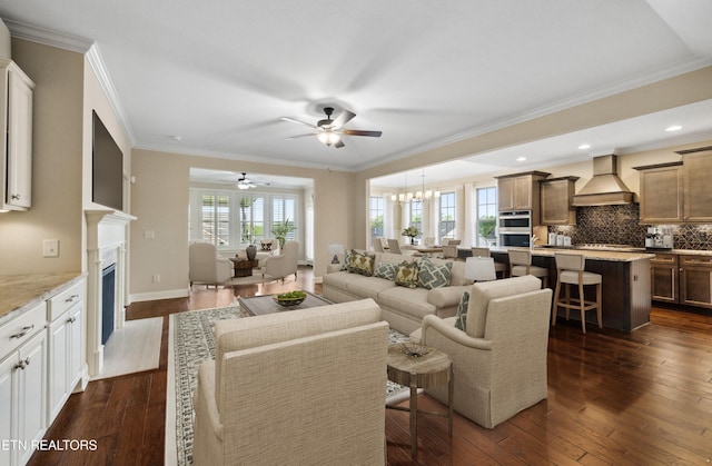 living room featuring a high end fireplace, crown molding, ceiling fan with notable chandelier, and dark wood-style floors