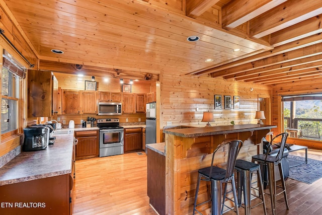 kitchen with wooden walls, a kitchen bar, recessed lighting, stainless steel appliances, and light wood finished floors