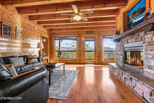 living area featuring beamed ceiling, a ceiling fan, a fireplace, and wood walls