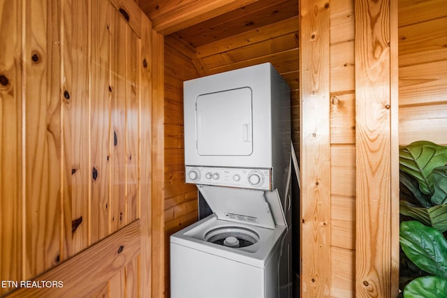 washroom featuring wooden walls, stacked washer / drying machine, laundry area, and wood ceiling
