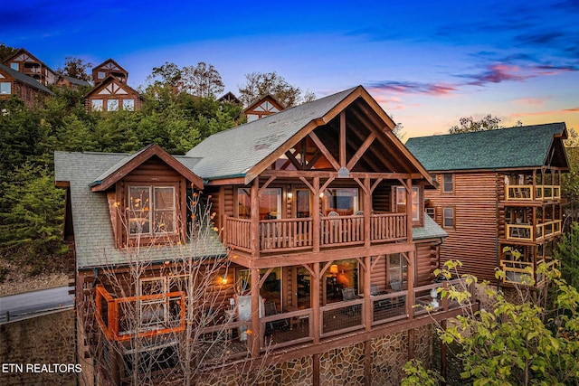 rear view of house featuring log exterior, a shingled roof, and a balcony
