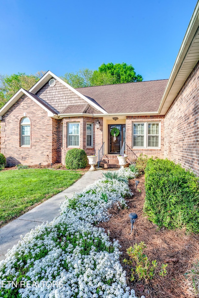 exterior space with brick siding, a lawn, and roof with shingles
