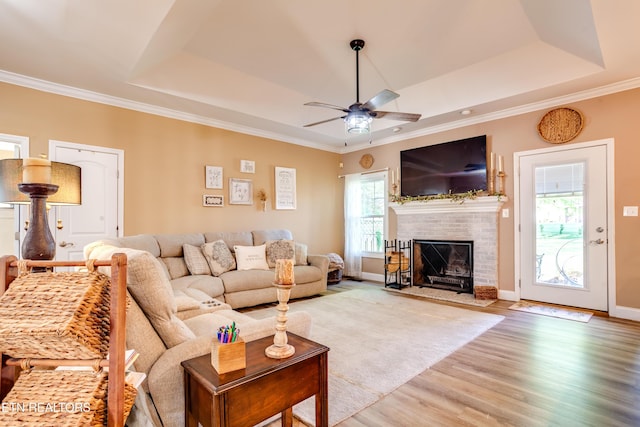 living room with a raised ceiling, ornamental molding, ceiling fan, a fireplace, and wood finished floors